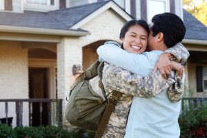 A young woman in uniform smiles as she hugs a young man tightly.